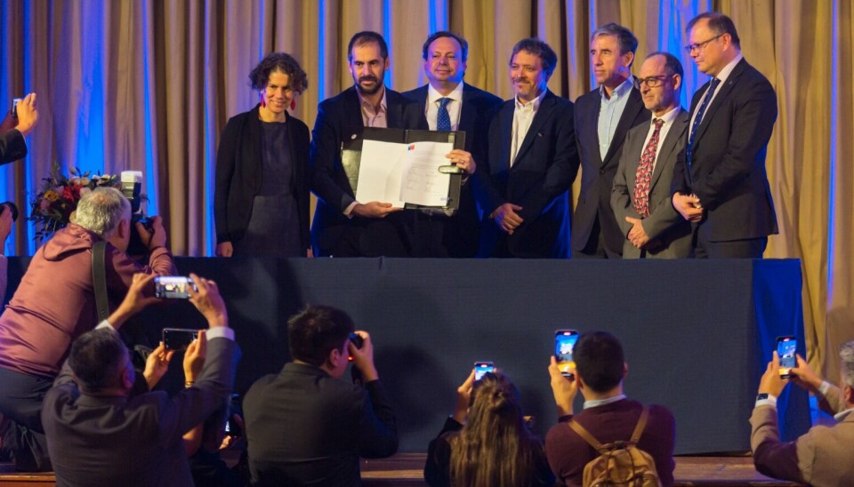 The voluntary agreement is displayed to journalists. Those behind the table include environment minister Maisa Rojas, left, and AquaChile general manager Sady Delgado, third from right.