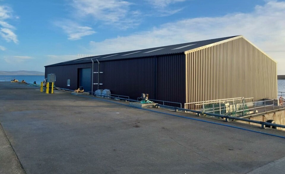 The large steel shed on the concrete hull of the Cooke feed barge, and inset, the barge on fire in January.